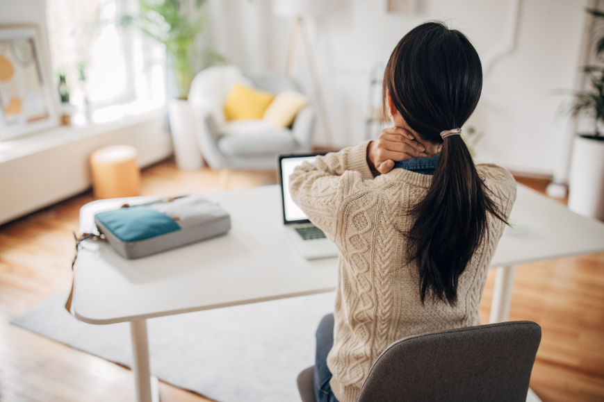 Tired woman massaging her neck after hours at a non-ergonomic laptop setup