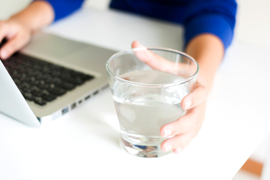 Glass of water reaching by hand of a man while working